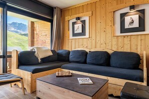 A wooden interior with a sofa, a table, and framed pictures on the wall. - “V6” by Versant Collection (Val Thorens)