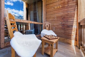A wooden cabin with a chessboard on a small table, a white furry chair, and a wooden ladder leaning against a window. - “V6” by Versant Collection (Val Thorens)