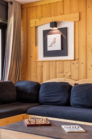A cozy living area with a wooden wall panel, a framed picture, a chessboard, and a magazine on a coffee table. - “V6” by Versant Collection (Val Thorens)