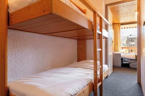 Ein kleines Zimmer mit Etagenbett, Schreibtisch und Bergblick durch ein Fenster.