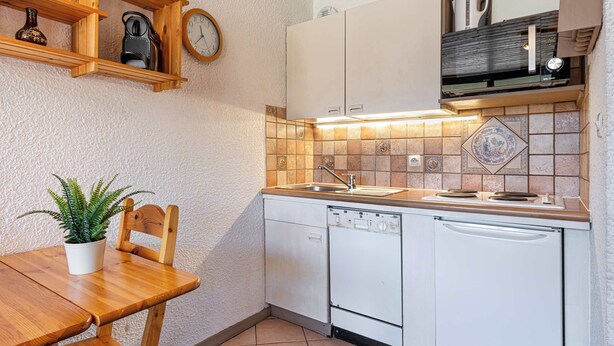 Una cocina compacta con estantes de madera, un reloj, un lavamanos y un lavavajillas.