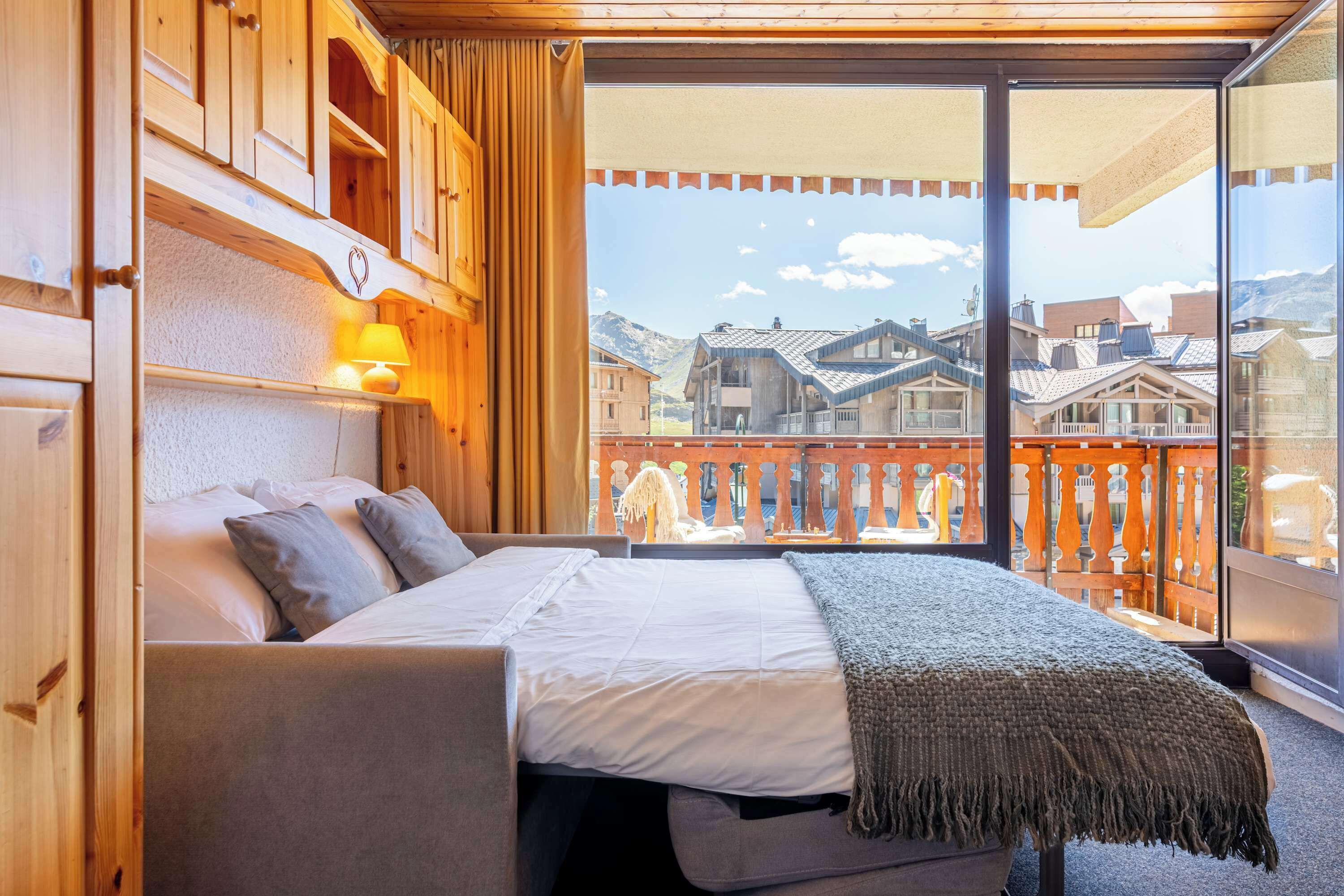 A bedroom with a bed, wooden headboard, and a view of buildings through a large window.