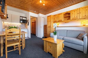 Ein gemütlicher Wohnbereich mit einem Holzesstisch, Stühlen, einem grauen Sofa und einem kleinen Holztisch mit einem Blumentopf.