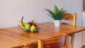 Una mesa de comedor de madera con un frutero, una planta en maceta y una cafetera sobre una estantería.