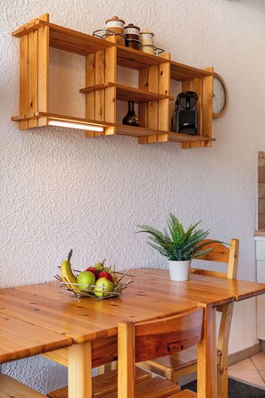 Ein Holztisch mit einer Obstschale, einer Blumentöpfe und einer Kaffeemaschine auf einem darüber befindlichen Regal.