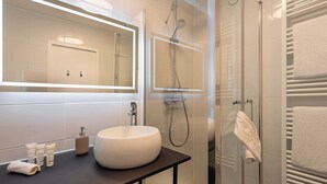 Un bagno moderno con un grande specchio, un lavandino rotondo, box doccia in vetro e porta asciugamani.
