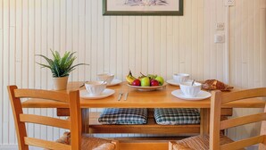 Un tavolo da pranzo con un quadro floreale incorniciato, una pianta in vaso e una ciotola di frutta.