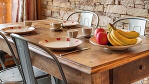 Una mesa de madera para comer con platos, tazas y un frutero. Un televisor está montado en la pared sobre la mesa.