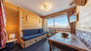 Una cabaña de madera acogedora con sofá, mesa de comedor y vistas panorámicas a la montaña.