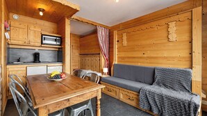 Interior de una cabaña de madera con una mesa de comedor, sillas, un microondas, un sofá y una pequeña cocina.
