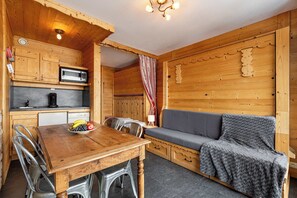 Ein Holzblockhaus-Interieur mit Esstisch, Stühlen, einer Mikrowelle, einer Couch und einer kleinen Küchenzeile.