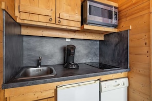 A compact kitchen with wooden cabinets, a stainless steel sink, a coffee maker, a microwave, and a dishwasher. - “V2” by Versant Collection (Val Thorens)
