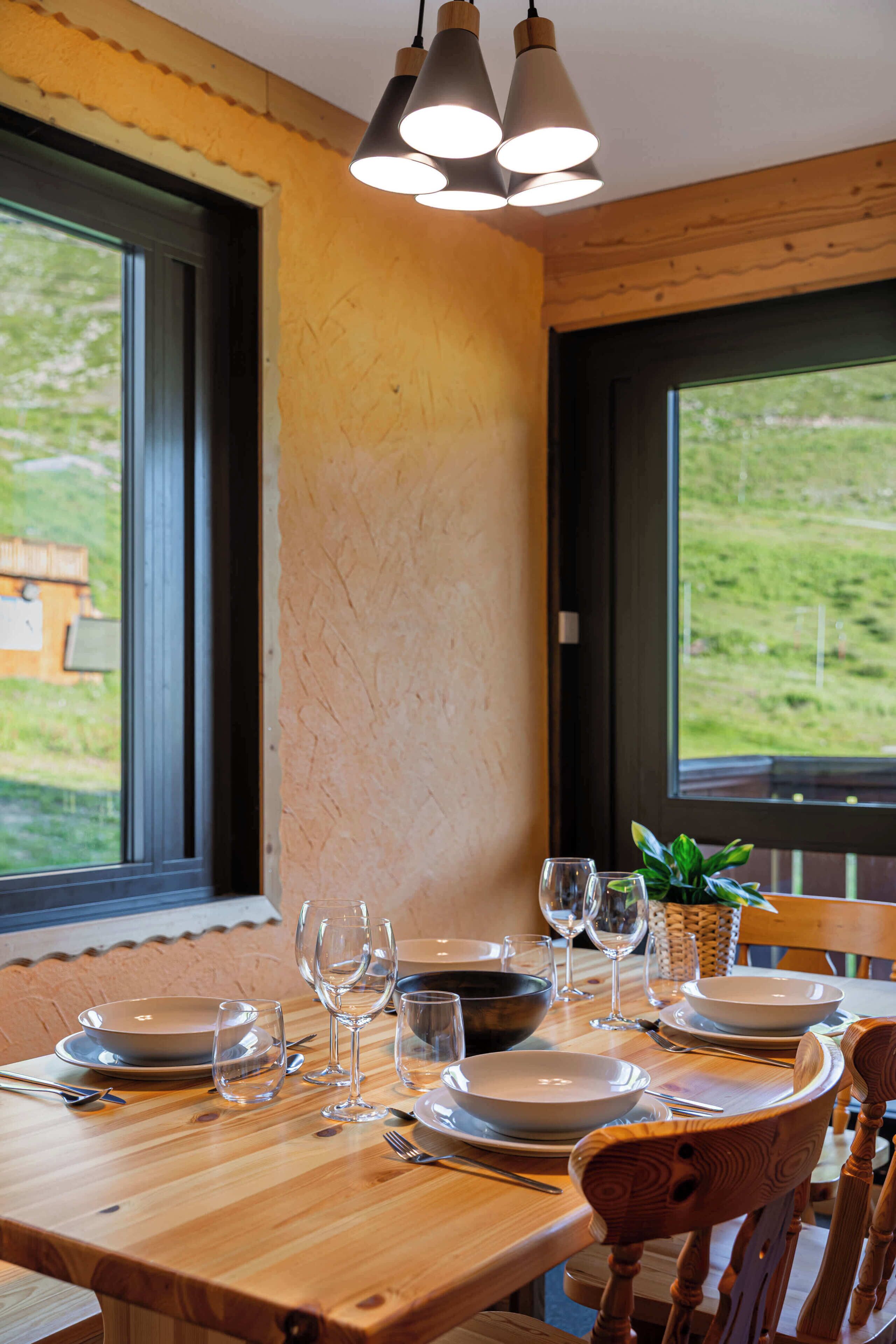 Een eettafel gedekt met borden, kommen en wijnglazen, met uitzicht op groen buiten door grote ramen.