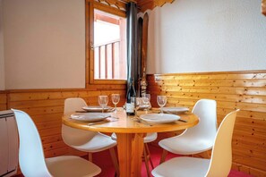 A wooden dining table with white chairs, a window with a view, and a ski pole leaning against the wall. - Residence Hermine, Ski In-Out with WiFi in Val Thorens, “V7” by Versant Collection (Val Thorens)