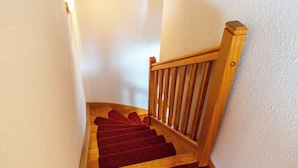 Eine Holztreppe mit rotem Teppich, weißen Wänden und einem Holnänder.