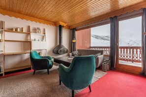 A cozy room with a wooden ceiling, a fireplace, a sofa, two chairs, a table, and a view of a snowy mountain. - Residence Hermine, Ski In-Out with WiFi in Val Thorens, “V7” by Versant Collection (Val Thorens)