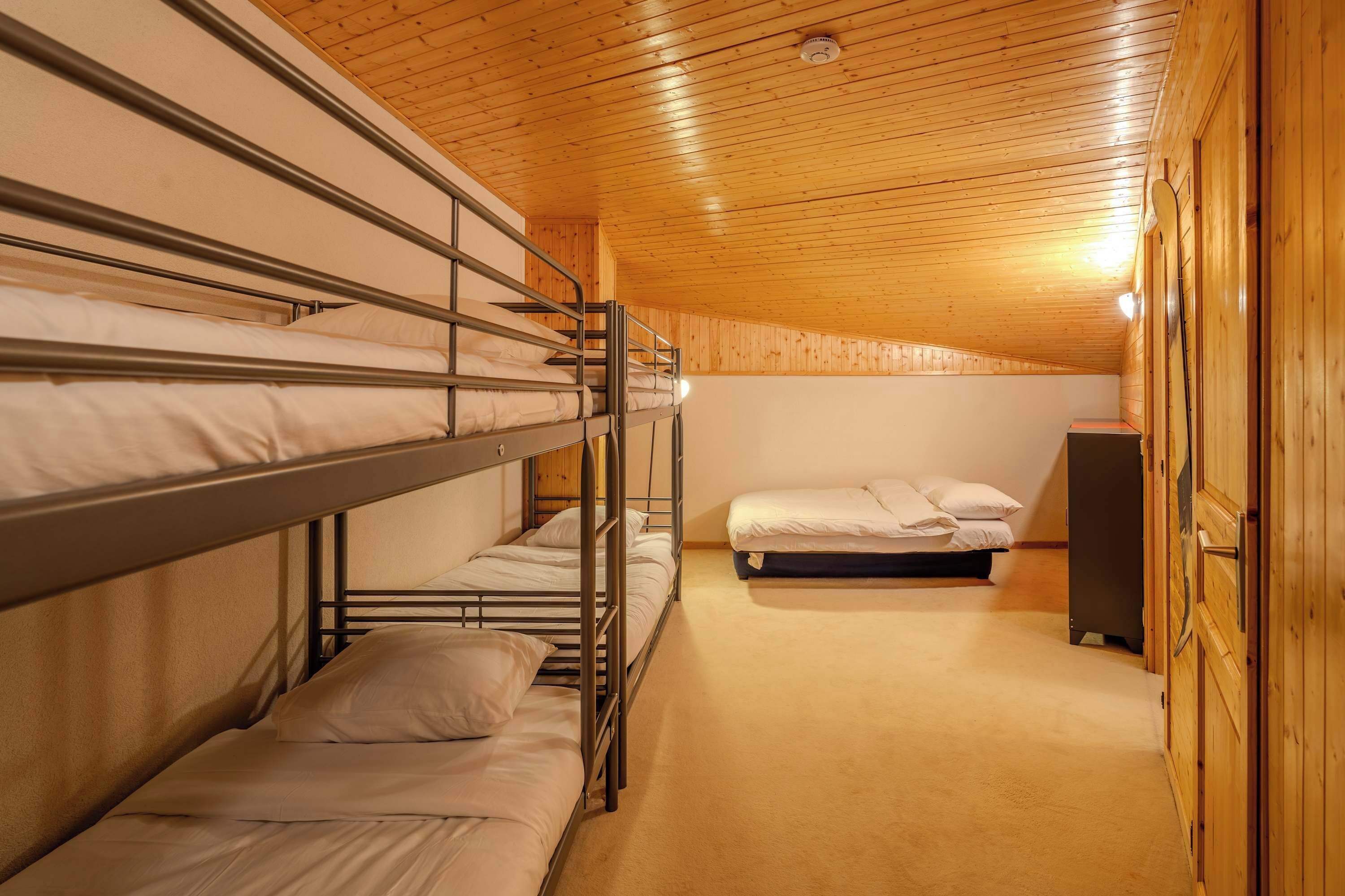 A bunk room with wooden walls and ceiling, a bunk bed, a single bed, and a wardrobe.