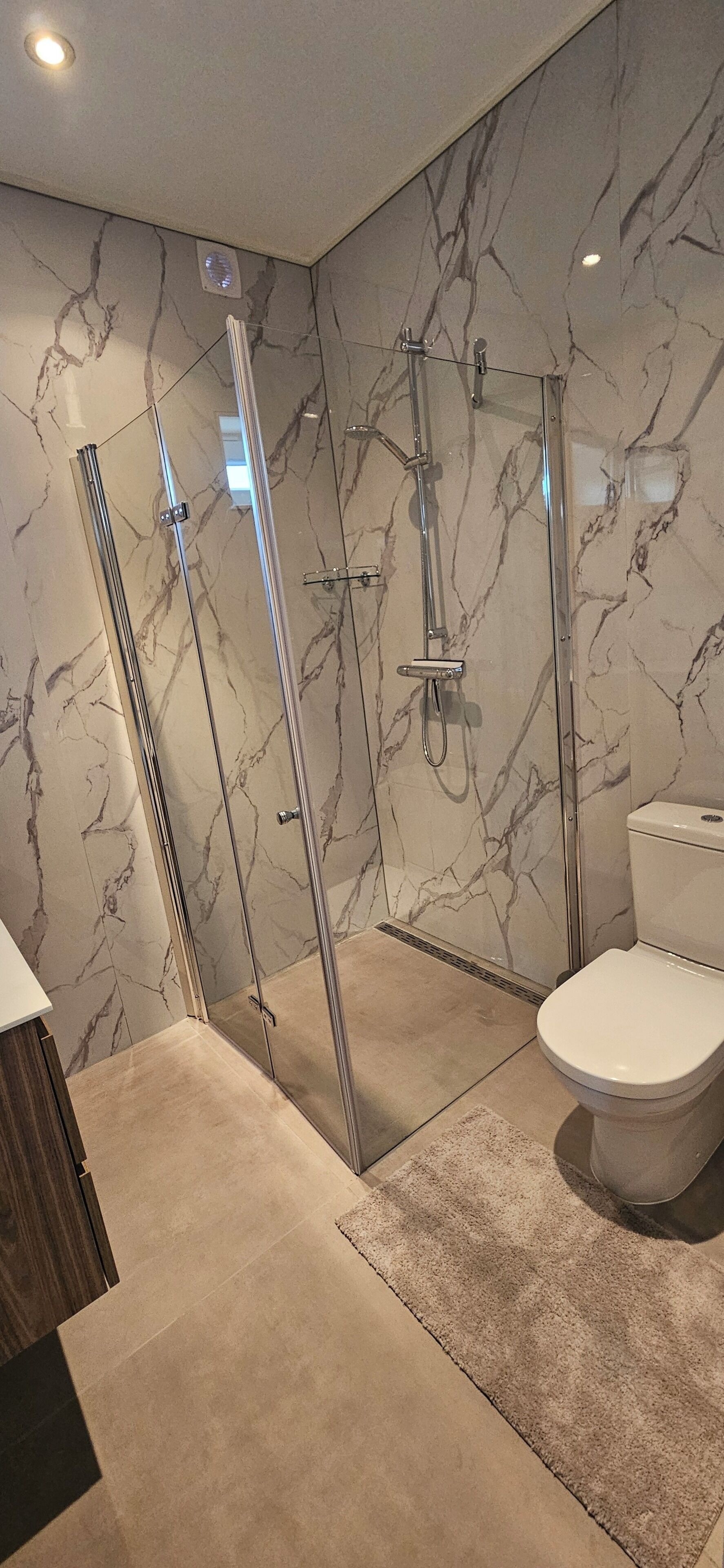 A bathroom with a glass-enclosed shower, a toilet, and marble walls.