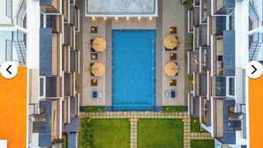 A modern hotel with a central swimming pool, multiple balconies, and outdoor seating areas.