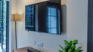 A modern living room with a flat-screen TV mounted on the wall, a wooden entertainment unit below, and a potted plant to the right.