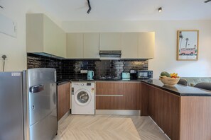 A compact kitchen with a washing machine, microwave, and a bowl of fruit on the counter. - La Vida 101 premium equipped boutique stay in Goa Calangute  (Calangute)
