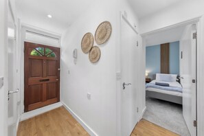 Un corridoio con una porta in legno, un muro bianco decorato con tre arazzi, e una camera da letto con un letto e un comodino.