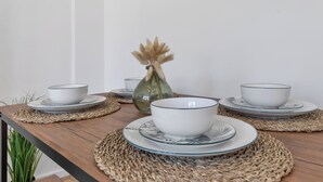 Une table à manger avec des assiettes et des bols blancs, un vase en verre contenant des fleurs séchées et un set de table en fibres tressées.