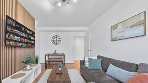 Un salon moderne avec un téléviseur à écran plat fixé à un mur en bois, un coin repas avec une table et des bancs, un canapé gris avec des coussins et une grande peinture abstraite accrochée au mur.
