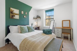A bedroom with a bed, bedside table, dresser, and a window with a view of buildings. - Spacious & Cosy Camden Town 3BR Sleeps 7! Only 10 Min to St Pancras Station! (London)
