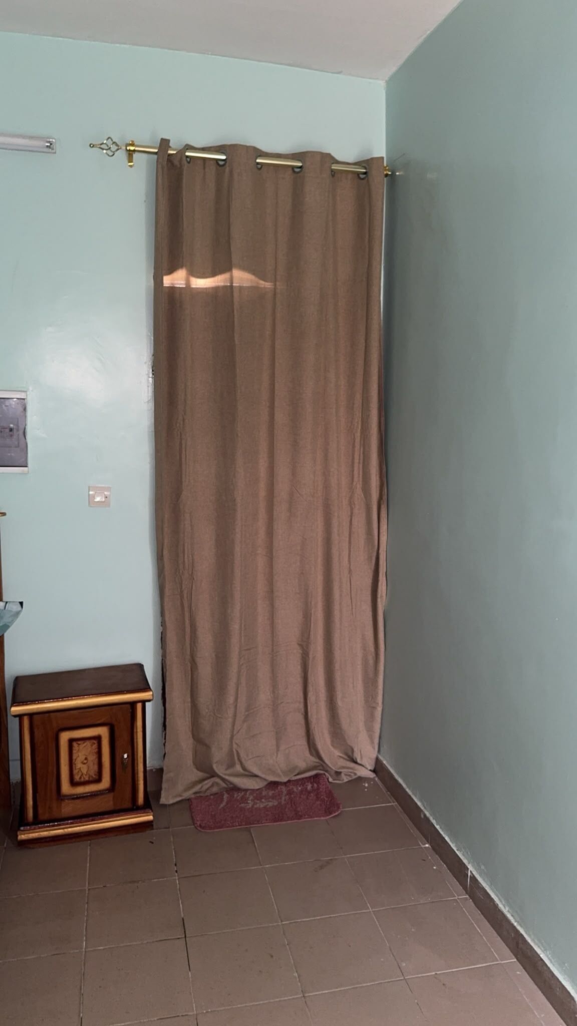 A room with a curtain, a small wooden cabinet, and a tiled floor.