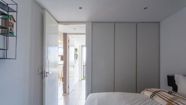 A bedroom with a bed, a wardrobe, a shelf with decorative items, and a door leading to another room. - Cosy retreat in Woodstock (Cape Town)