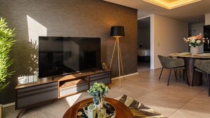 A modern living room with a flat-screen TV, a standing lamp, a dining area with chairs, and a decorative plant. - Cosy retreat in Woodstock (Cape Town)