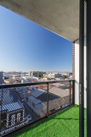 Un balcon donnant sur un paysage urbain, un parking et un immeuble à la façade jaune.