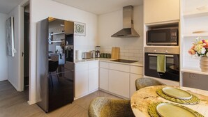 A modern kitchen with white cabinetry, a stainless steel refrigerator, a Bosch oven, and a microwave. - Cosy retreat in Woodstock (Cape Town)