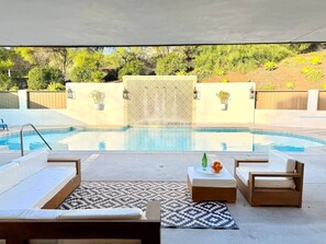 Un espace extérieur avec une piscine, des chaises longues, un tapis à motifs et un mur décoratif.