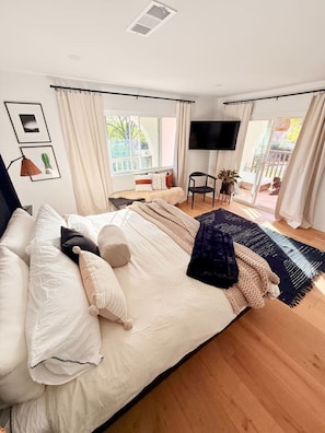 A bedroom with a large bed, a TV mounted on the wall, and a view of the outdoors through the window. - Lavender House + Guest Suite - Sleeps 11 (Ojai)
