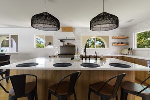 Une cuisine moderne dotée d’un grand îlot central, de luminaires suspendus noirs et de chaises en bois.