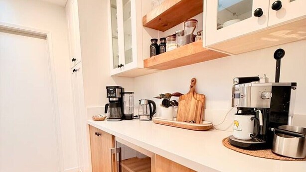 Una cocina moderna con armarios blancos, una cafetera y una tabla de cortar de madera.