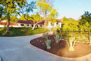 A courtyard with a paved walkway, a metal fence, and a building with a red-tiled roof. - Lavender House + Guest Suite - Sleeps 11 (Ojai)