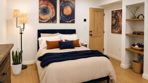 Un dormitorio con una cama, lámparas de noche, una planta en maceta y obras de arte en las paredes.