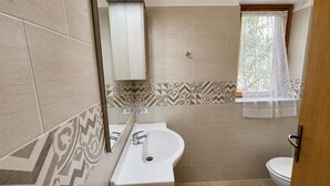 Et badeværelse med vask, spejl, toilet og tapetserede fliser.