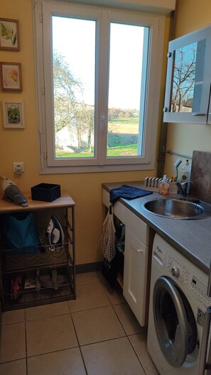 A compact kitchen with a washing machine, a sink, and a window with a view of a green landscape. - Modern Normandy House 7 Bedrooms sleeps 14 (Barenton)
