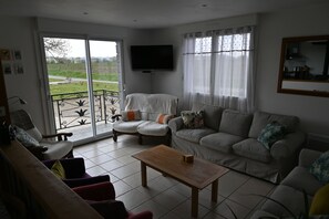 A living room with a sofa, armchairs, a coffee table, a TV mounted on the wall, and a balcony with a view of the outdoors. - Modern Normandy House 7 Bedrooms sleeps 14 (Barenton)