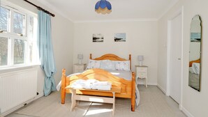 A bedroom with a wooden bed, two bedside tables, a nightstand, a window with curtains, a wall-mounted mirror, and two framed pictures. - Cosy Aberdeenshire Stone Cottage (Inverurie)