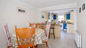 A dining area with a table and chairs, a kitchen with blue cabinets, and a view of the living area. - Cosy Aberdeenshire Stone Cottage (Inverurie)