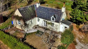 A two-story house with a sloped roof, a visible chimney, and a small garden area. - Cosy Aberdeenshire Stone Cottage (Inverurie)