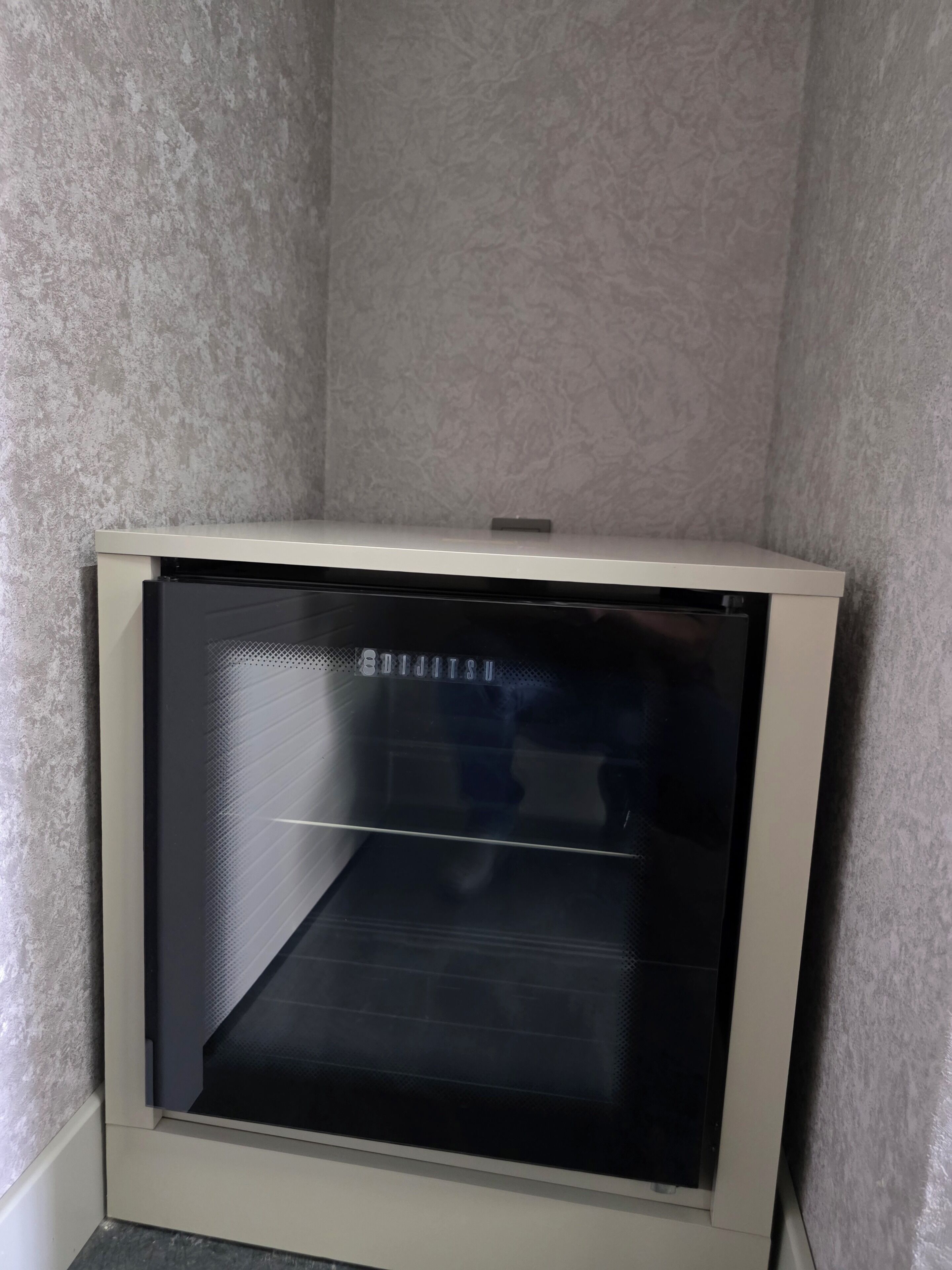 Un angolo di una stanza con un armadietto bianco e un elettrodomestico nero, forse un frigorifero o un forno, con una parete strutturata sullo sfondo.