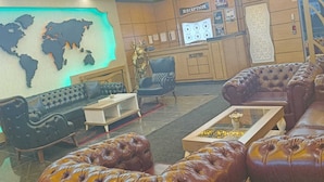 Un hall con sofás de cuero, una mesa de recepción, un mapa mundial y un candelabro.
