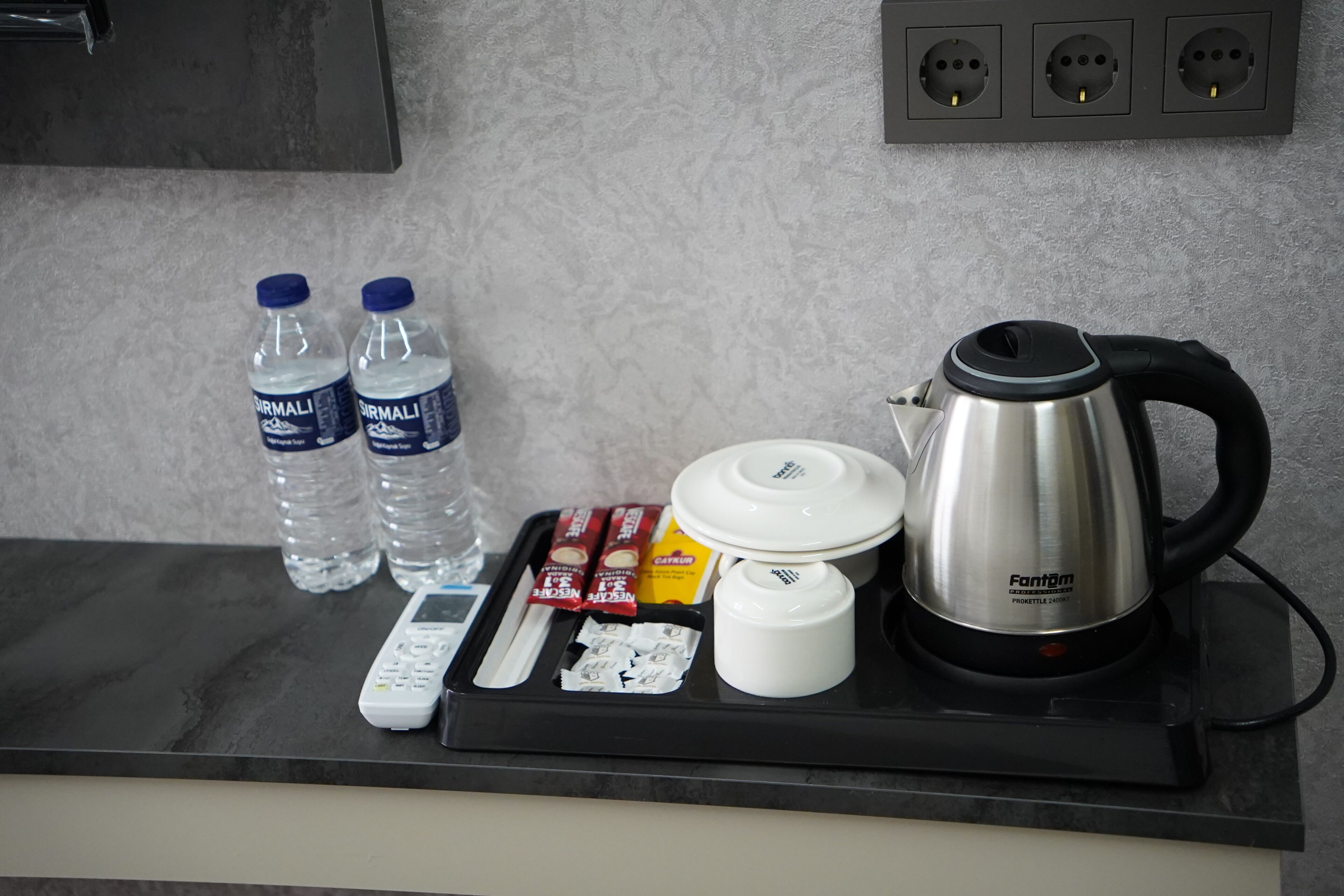Una encimera de cocina con una tetera, botellas de agua, un control remoto y una bandeja con comida.