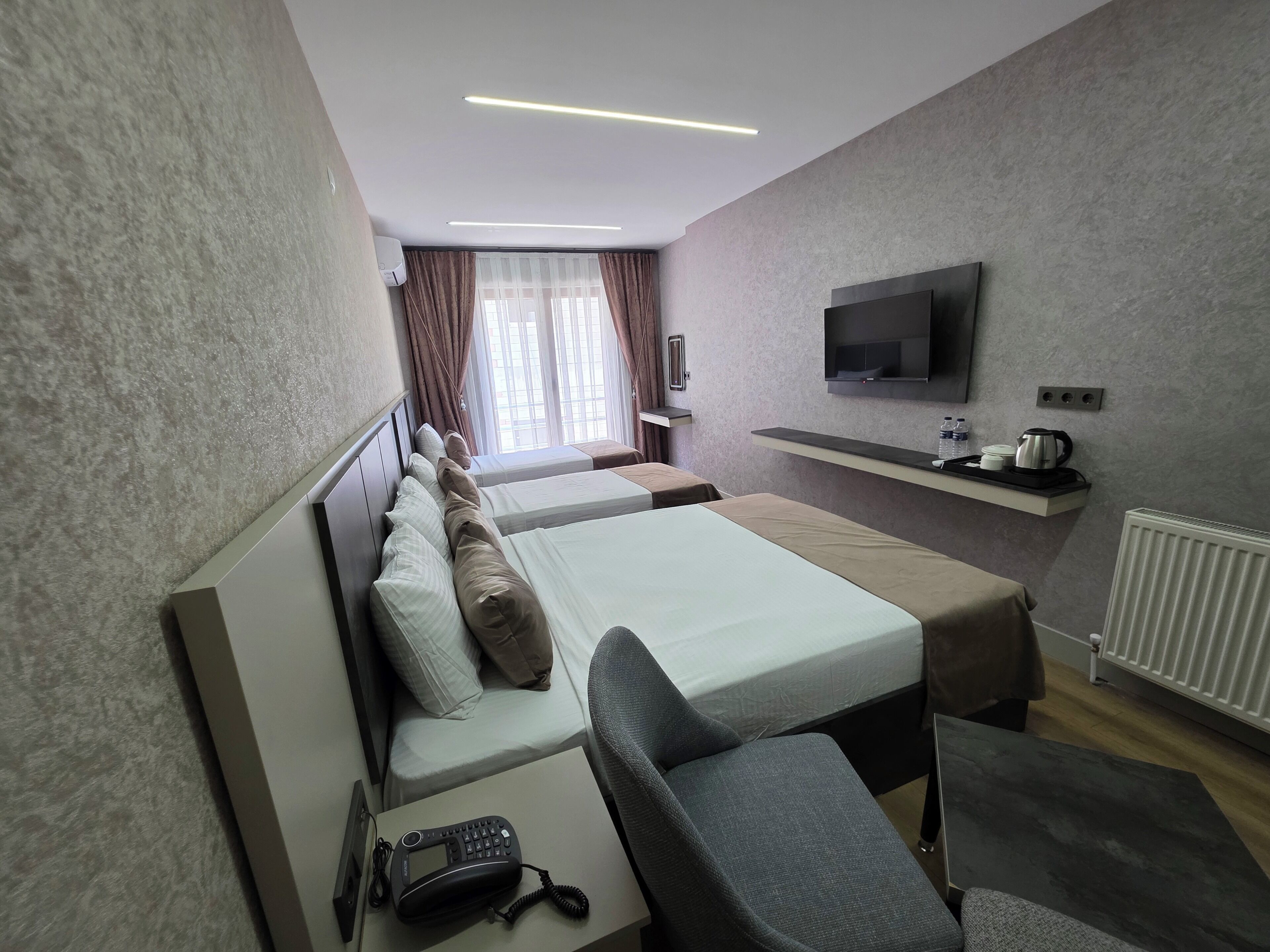 A hotel room with two beds, a TV, a phone, and a small table with a kettle.